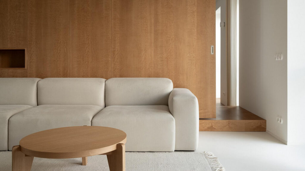 Jasna sofa przy drewnianej ścianie z okrągłym stolikiem